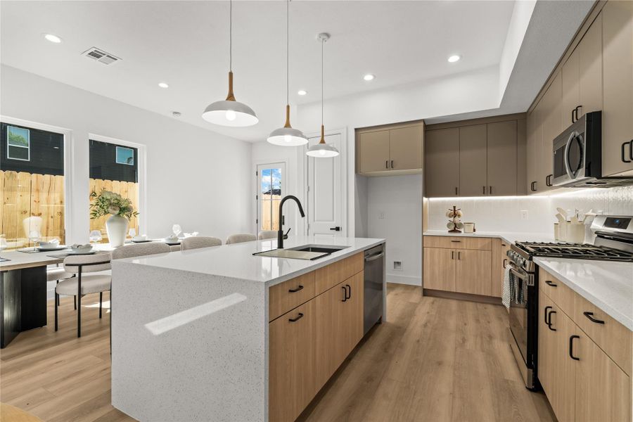 The large kitchen island anchors the room and features a breakfast bar that leads into a separate dining area. Light oak flooring runs throughout the entire space, and three modern white-and-wood pendant lights hang overhead to light up the main floor.