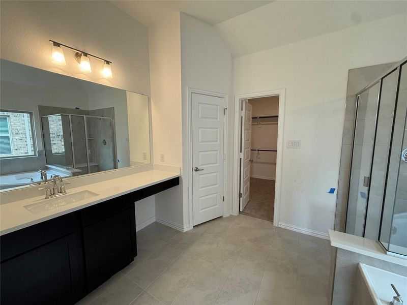 Full bathroom with a shower stall, a garden tub, a spacious closet, vanity, and light tile patterned floors Full bathroom with a shower stall, a garden tub, a spacious closet, vanity, and light tile patterned floors