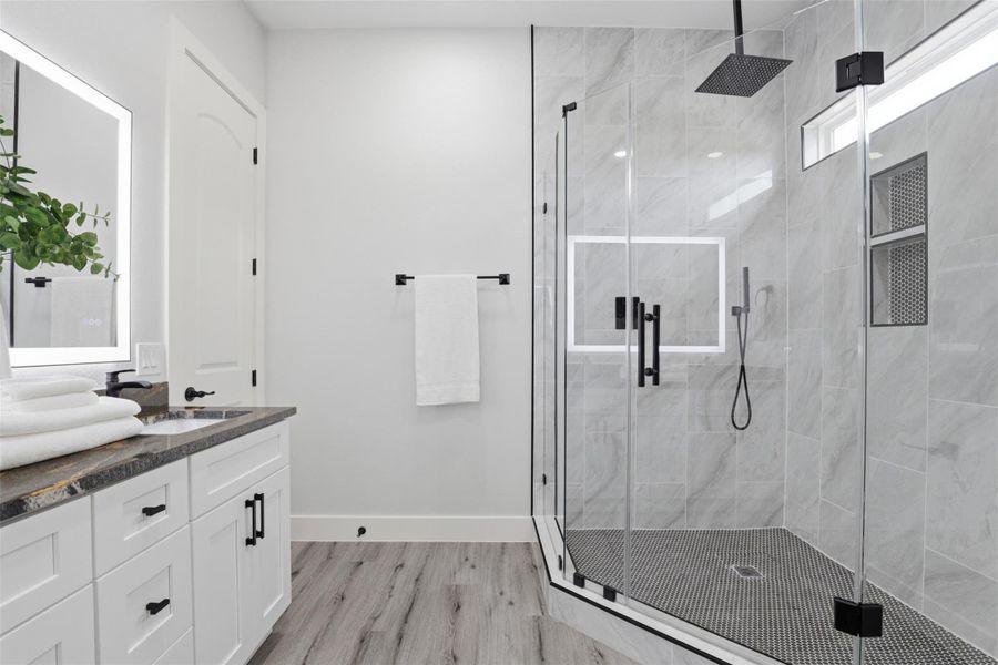 Bathroom featuring a frameless glass shower enclosure with matte black hardware, dual shower niches, and a rainfall showerhead