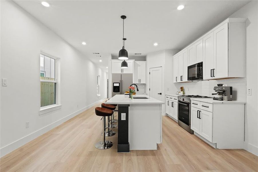 Kitchen featuring white cabinetry, pendant lighting, appliances with stainless steel finishes, an island with sink, and a kitchen breakfast bar