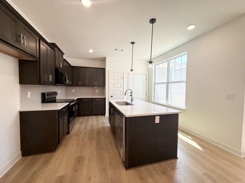 Kitchen with stainless steel appliances, light stone counters, an island with sink, and light wood finished floors