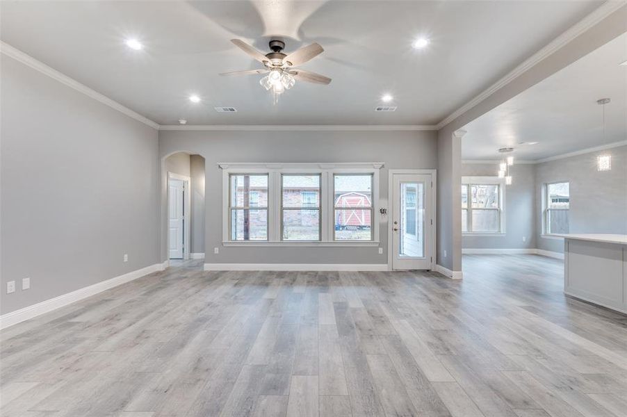 Unfurnished living room featuring crown molding, ceiling fan, and light wood-type flooring