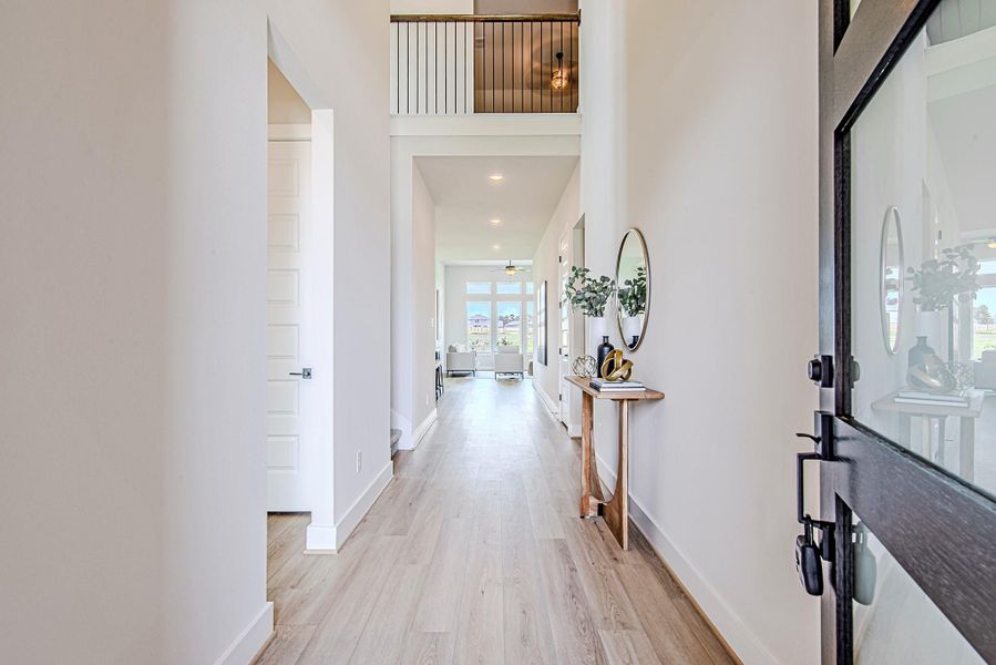 Step through the modern glass door into a light-filled entryway with soaring ceilings, clean lines, and a view that draws your eyes straight to the back windows and water beyond.
