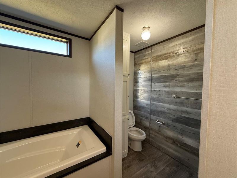 Bathroom with a textured ceiling, dark wood finished floors, a bath, wooden walls, and ornamental molding