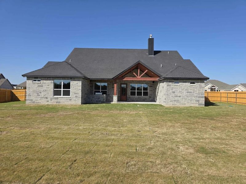 Rear view of house with a fenced backyard, a patio area, a chimney, and stone siding Rear view of house with a fenced backyard, a patio area, a chimney, and stone siding