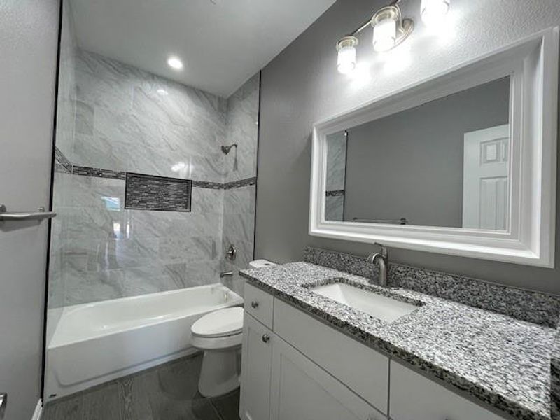 Full bathroom featuring bathtub / shower combination, granite top vanity, and ceramic wood look flooring Full bathroom featuring bathtub / shower combination, granite top vanity, and ceramic wood look flooring