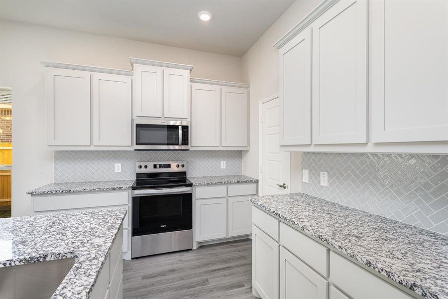 Kitchen featuring white cabinets, light wood-type flooring, stainless steel appliances, and tasteful backsplash