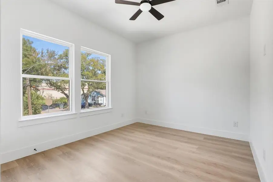 Bright room featuring wood-finish flooring, white walls, and a ceiling fan Bright room featuring wood-finish flooring, white walls, and a ceiling fan