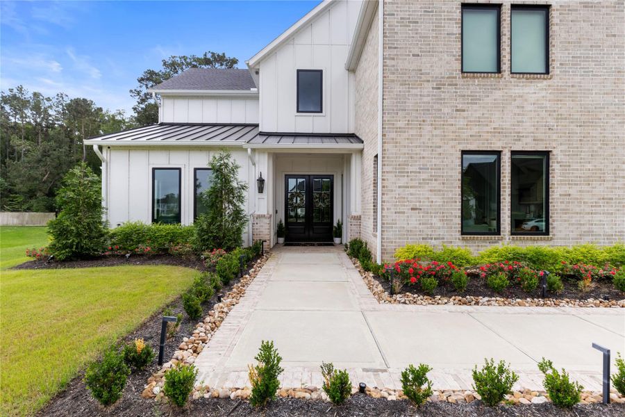 The front approach highlights the home’s clean architectural lines, black framed windows, and inviting covered entry with prestine professionally designed landscaping.