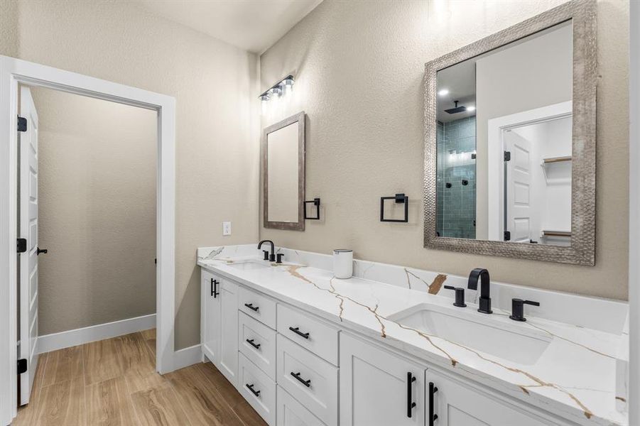 Double vanity featuring white cabinetry, quartz countertops with prominent veining, and integrated sinks