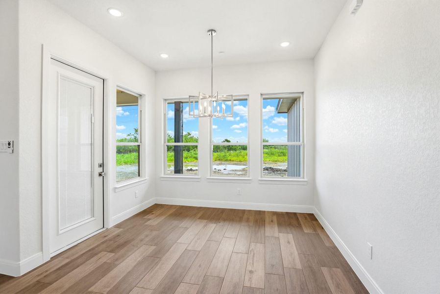 The wood-look tile flooring complements the modern chandelier in this well-lit dining area.