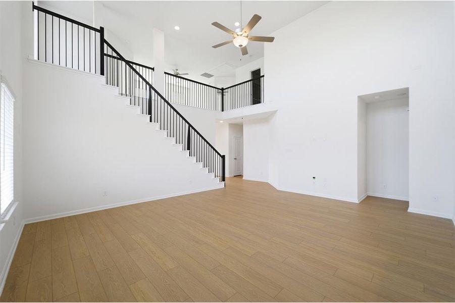 Unfurnished living room with ceiling fan, light wood-style floors, and a high ceiling