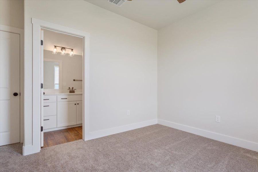 A well-lit bedroom features plush carpeting and a convenient en-suite bathroom with a modern vanity.