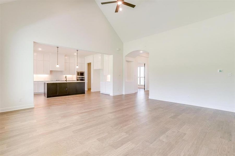 Unfurnished living room featuring sink, high vaulted ceiling, ceiling fan, and light wood-type flooring