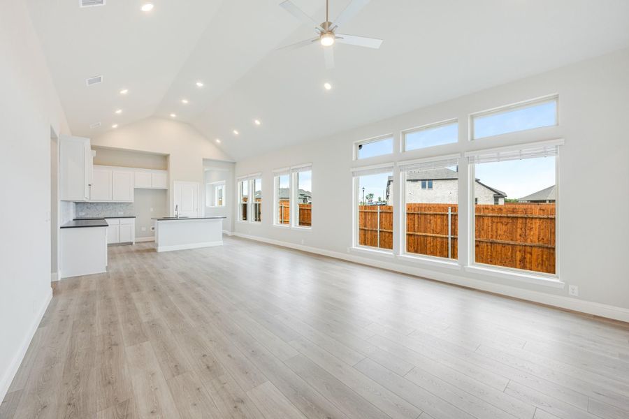 Open living area with vaulted ceiling, hardwood floors, and large windows, with kitchen visible in background