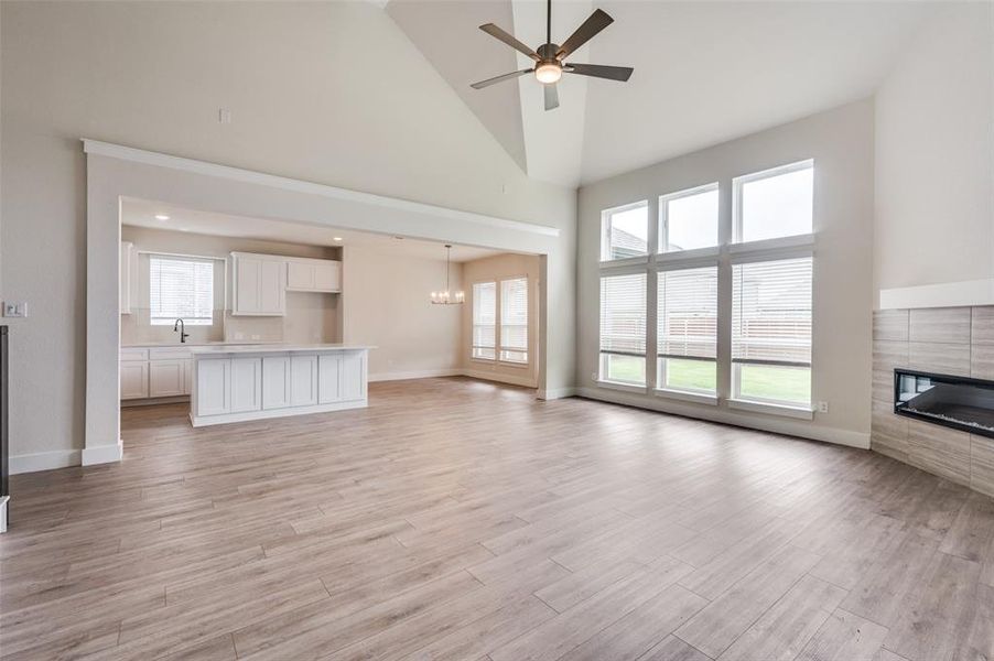 Unfurnished living room featuring high vaulted ceiling, a tiled fireplace, a ceiling fan, healthy amount of natural light, and light wood-style flooring Unfurnished living room featuring high vaulted ceiling, a tiled fireplace, a ceiling fan, healthy amount of natural light, and light wood-style flooring
