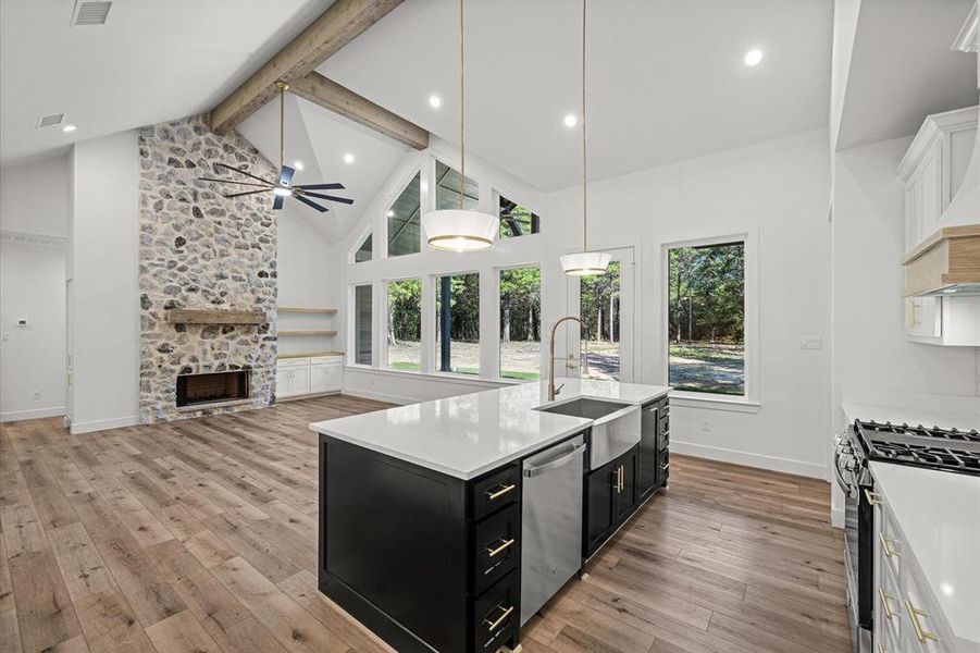 Kitchen featuring custom cabinetry, beam ceiling, hanging light fixtures, high vaulted ceiling, and an island with sink