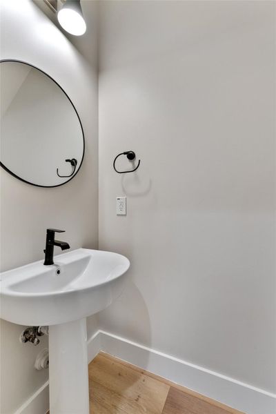 Half bath downstairs. Pedestal sink with matte black faucet, complemented by a round wall-mounted mirror and coordinating towel ring Half bath downstairs. Pedestal sink with matte black faucet, complemented by a round wall-mounted mirror and coordinating towel ring