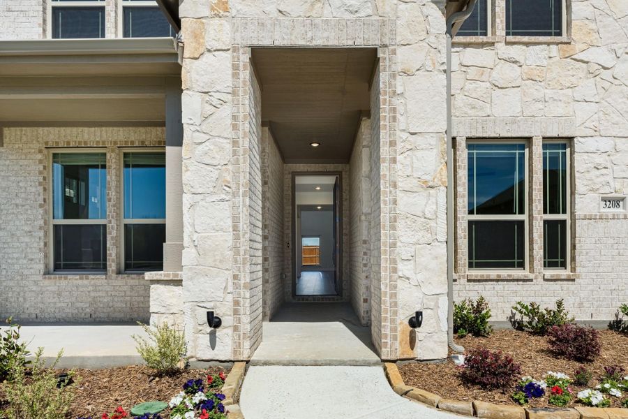 Home entrance with stone and brick exterior, covered walkway leading to front door with landscaping