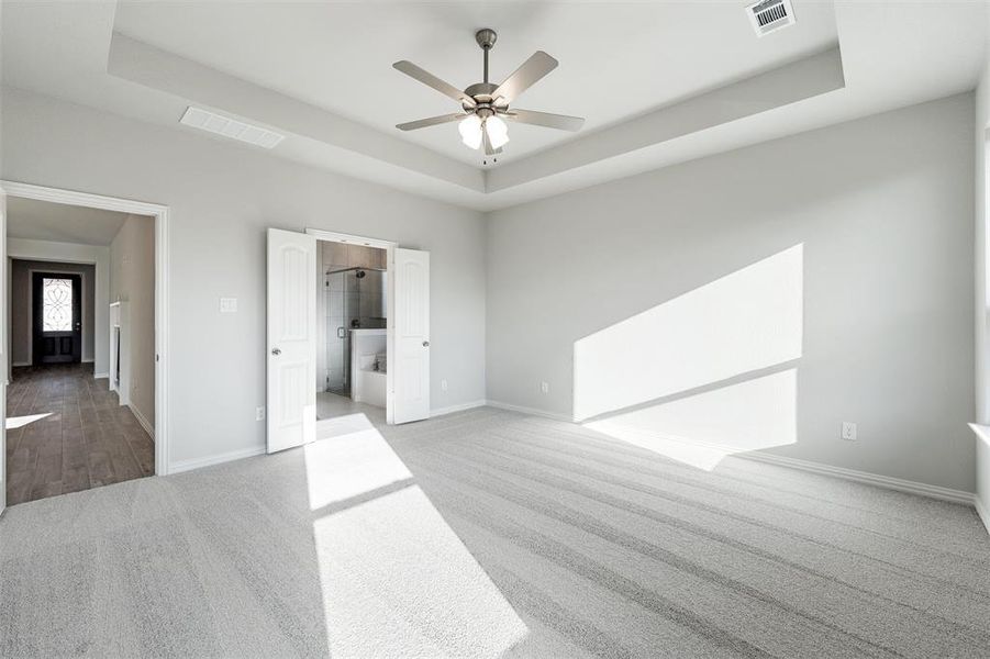 Unfurnished bedroom with a raised ceiling, connected bathroom, carpet flooring, and a ceiling fan