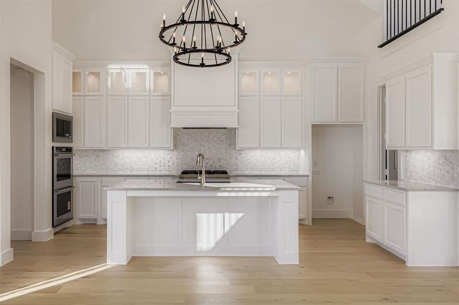Kitchen featuring tasteful backsplash, white cabinets, light stone countertops, light wood-style floors, and high vaulted ceiling Kitchen featuring tasteful backsplash, white cabinets, light stone countertops, light wood-style floors, and high vaulted ceiling