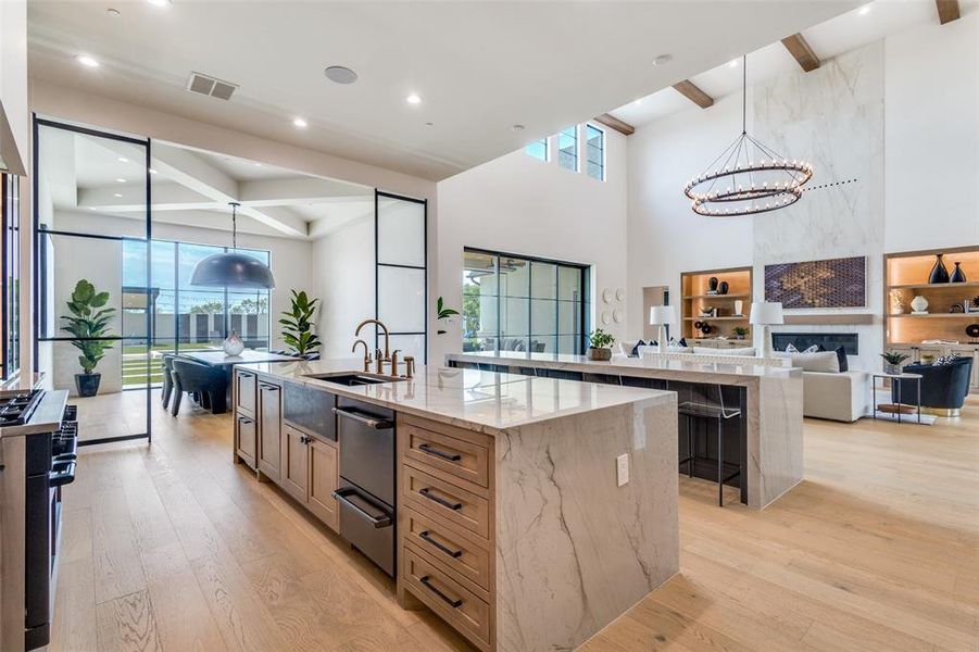 Kitchen featuring a large island with sink, light stone countertops, light wood-type flooring, sink, and pendant lighting