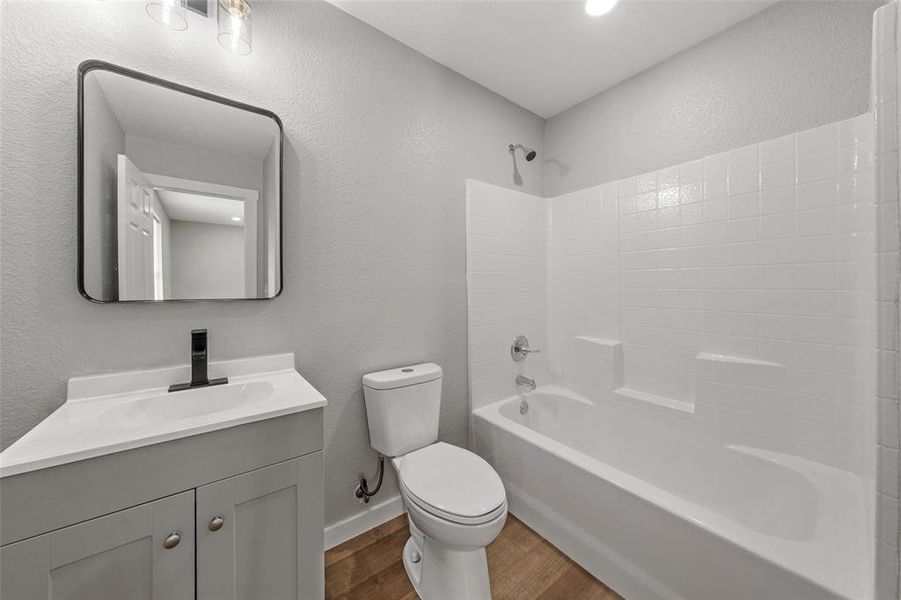 Bathroom featuring wood finished floors, vanity, washtub / shower combination, and a textured wall Bathroom featuring wood finished floors, vanity, washtub / shower combination, and a textured wall