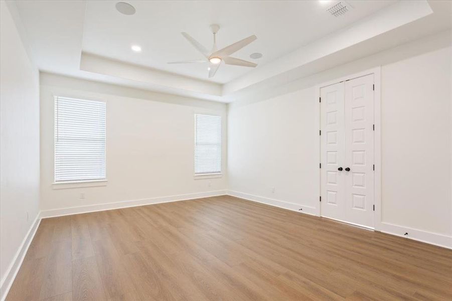 Spare room featuring a raised ceiling, wood finished floors, ceiling fan, recessed lighting, and healthy amount of natural light