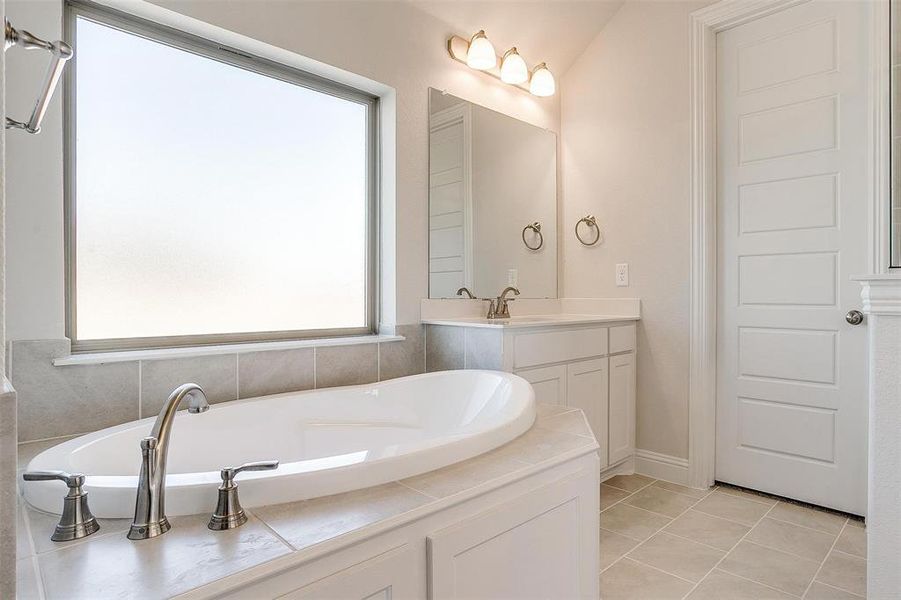 Bathroom with vaulted ceiling, vanity, tile patterned flooring, and a washtub