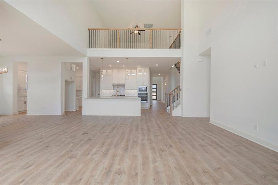 Spacious open-concept living area featuring light wood-finish flooring, a two-story vaulted ceiling, and a modern kitchen with a large island
