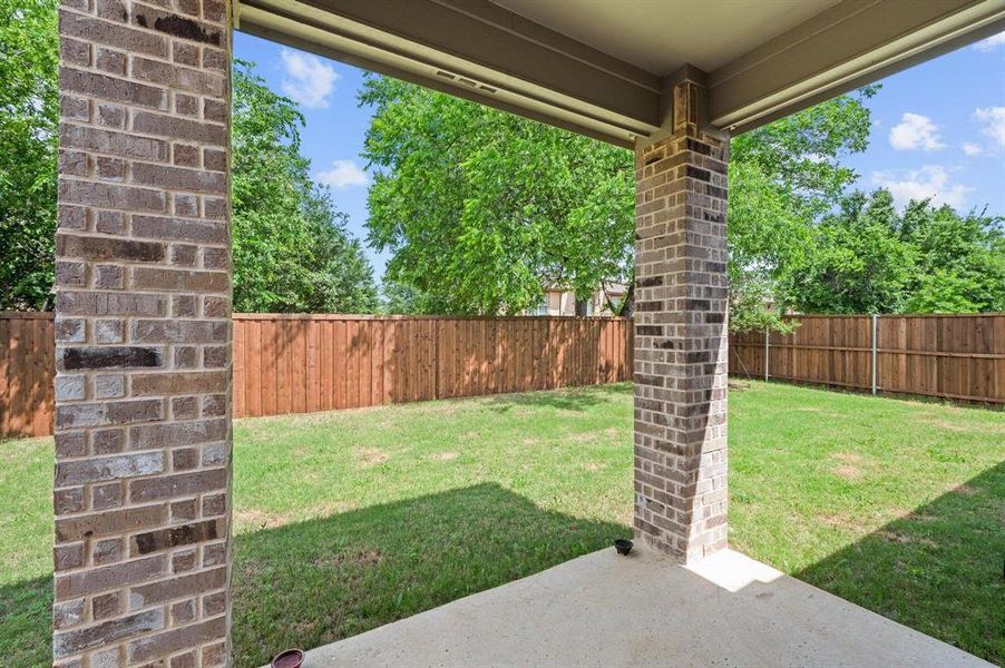 Covered patio with concrete flooring, brick columns, and a grassy backyard Covered patio with concrete flooring, brick columns, and a grassy backyard