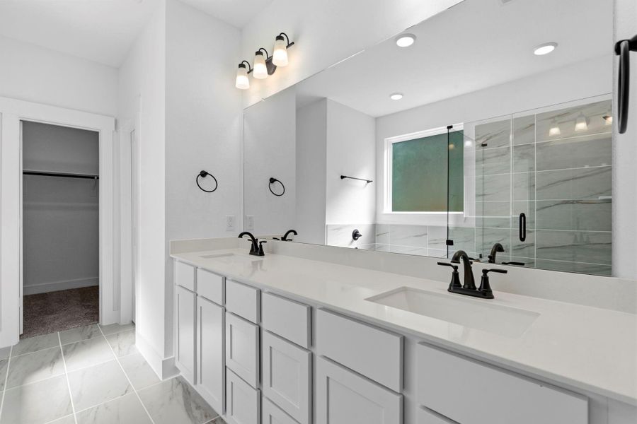 A dual vanity with ample counter space and elegant cabinetry provides plenty of room for two, with large mirrors and modern lighting that make the space feel bright and open.