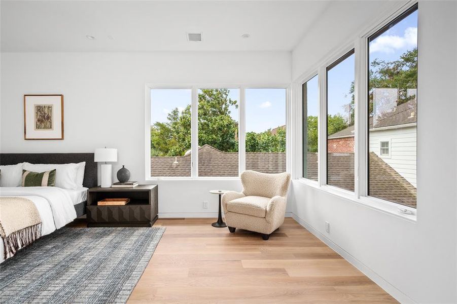 The focal point of this serene primary suite is the large corner windows that fill the room with natural light. The open doorway leads to a walk-in closet and ensuite bath, enhancing the flow and functionality of this luxurious space.