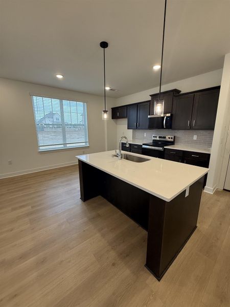 Kitchen featuring hanging light fixtures, stainless steel appliances, an island with sink, light wood-type flooring, and a breakfast bar