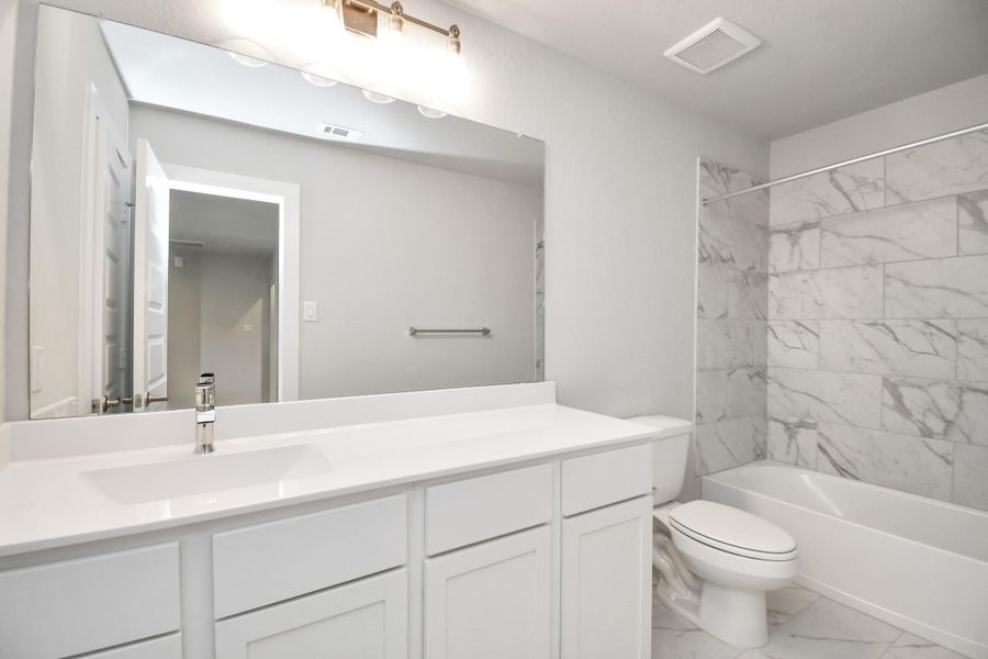 Secondary bath features tile flooring, bath/shower combo with tile surround, light stained wood cabinets, beautiful light countertop. Sample photo of completed home with similar floor plan. Actual colors and selections may vary.