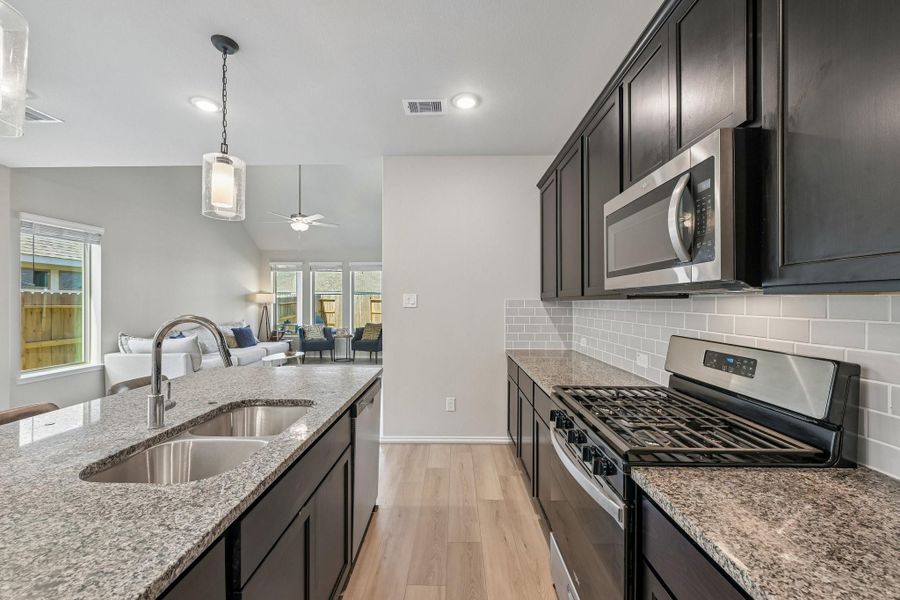 Modern kitchen with sleek granite countertops, stainless steel appliances, and dark wood cabinetry, opening to a bright living area with large windows.