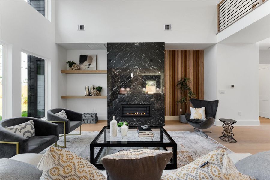 This modern living room features an open floor plan with high ceilings and a mezzanine. A striking black granite fireplace serves as a focal point, complemented by light wood flooring and accents. The space is airy and bright, ideal for both relaxing and entertaining. This modern living room features an open floor plan with high ceilings and a mezzanine. A striking black granite fireplace serves as a focal point, complemented by light wood flooring and accents. The space is airy and bright, ideal for both relaxing and entertaining.