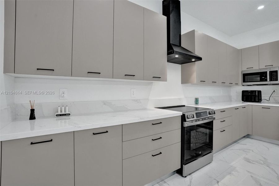 Contemporary kitchen featuring light gray cabinetry, white countertops, stainless steel appliances, and a black range hood