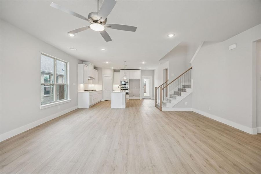Unfurnished living room with stairs, light wood-style floors, ceiling fan, and recessed lighting Unfurnished living room with stairs, light wood-style floors, ceiling fan, and recessed lighting