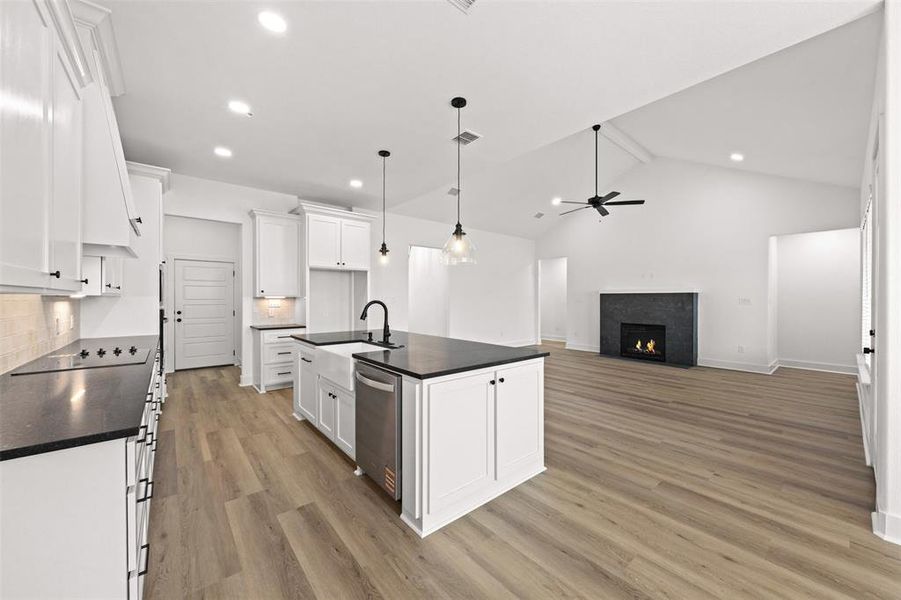 Kitchen with white cabinetry, a center island with sink, a fireplace with flush hearth, pendant lighting, and backsplash