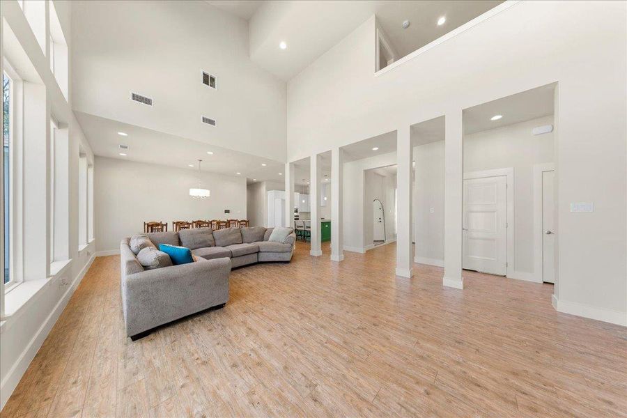 Living area with light wood-style floors, recessed lighting, and a towering ceiling Living area with light wood-style floors, recessed lighting, and a towering ceiling