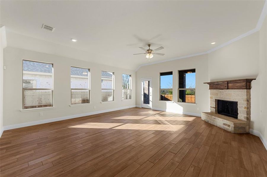 Unfurnished living room featuring vaulted ceiling, ceiling fan, crown molding, hardwood / wood-style flooring, and a fireplace