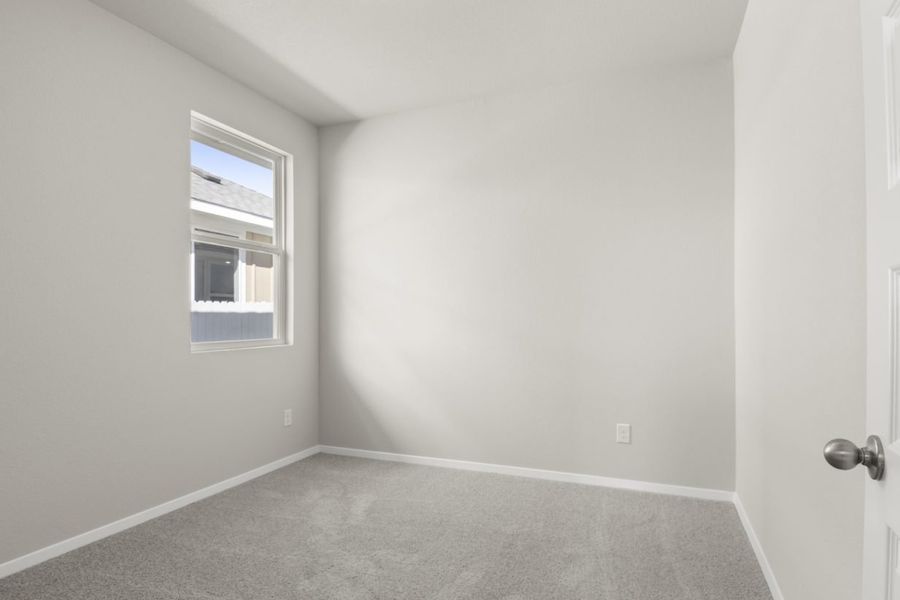 Image of a bedroom with light grey walls, tan carpeting, a window and white trim