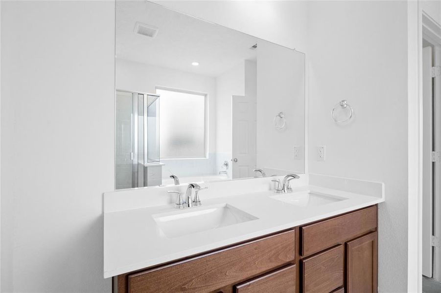 This primary bathroom offers room for everyone! Featuring stained cabinets with light countertops, high ceilings, custom paint, sleek and dark modern finishes.