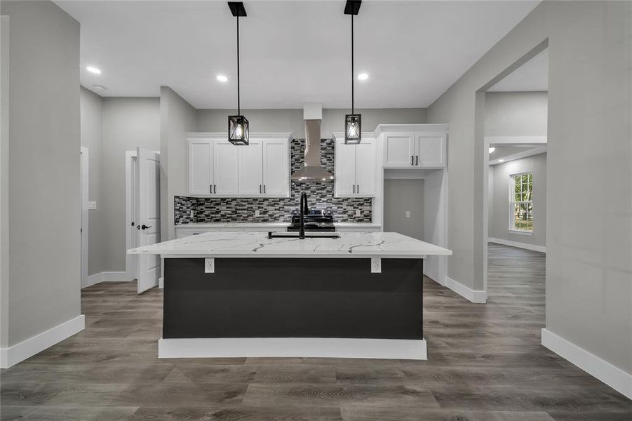 Kitchen featuring white cabinetry, light stone counters, an island with sink, wall chimney exhaust hood, and hardwood / wood-style flooring