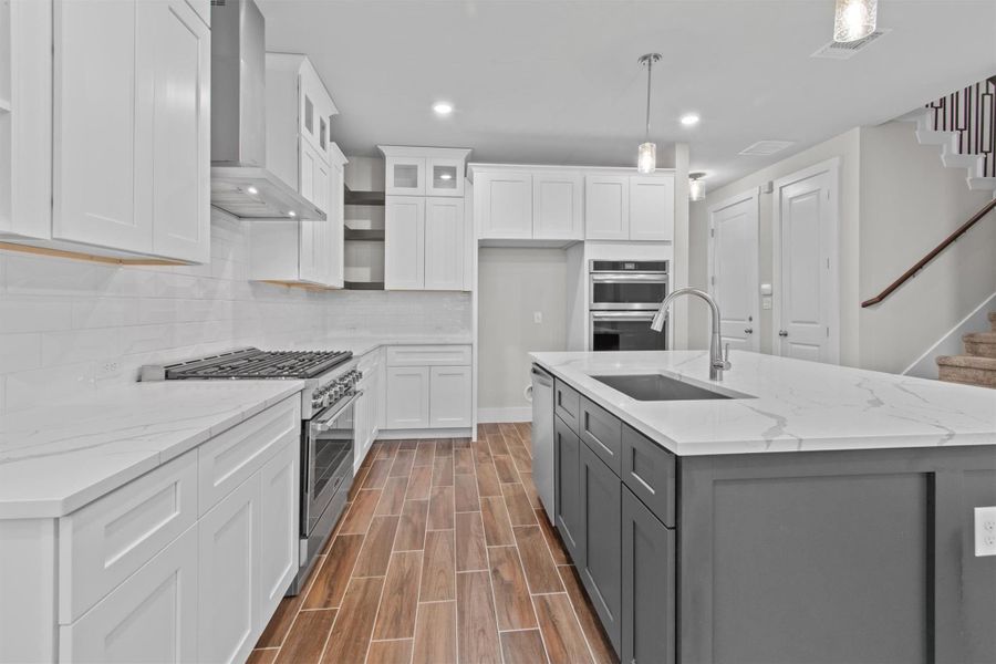 Kitchen with white cabinetry, decorative light fixtures, wall chimney range hood, and appliances with stainless steel finishes