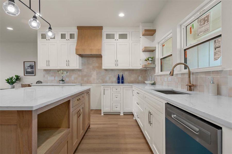 Kitchen featuring white upper and lower cabinetry, a natural wood-finish island with a light-toned countertop, a stainless steel dishwasher, a single basin sink with a curved faucet, and wood-finish flooring