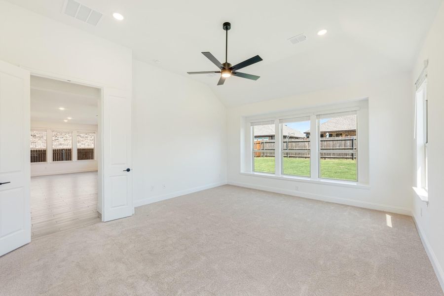 Empty bedroom with vaulted ceiling, ceiling fan, carpet flooring, and large window overlooking backyard Empty bedroom with vaulted ceiling, ceiling fan, carpet flooring, and large window overlooking backyard