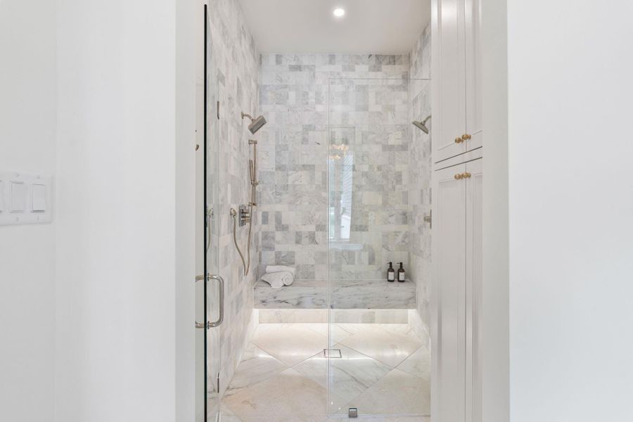 The walk-in shower makes a statement with floor-to-ceiling marble tile, a built-in bench, and dual showerheads for a true spa experience. Glass enclosure keeps the look open and seamless, while custom cabinetry provides additional storage just outside the shower. Thoughtful detailing and upgraded fixtures elevate every finish.