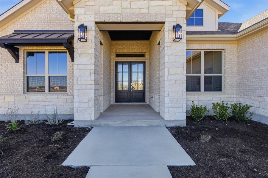 View of exterior entry featuring stone siding, french doors, a standing seam roof, and brick siding